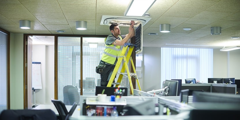Integral engineer on step ladder checking air conditioning in office
